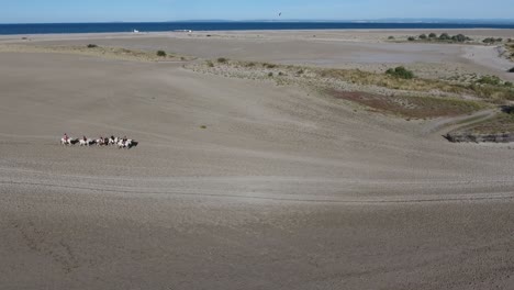 A-group-of-horse-riders-on-a-beach-shot-by-drone,-sunny-afternoon-France.